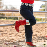 Person wearing a red sweater, black pants, and red boots standing near a round pen showing off Lucky Chuck Boot Socks.